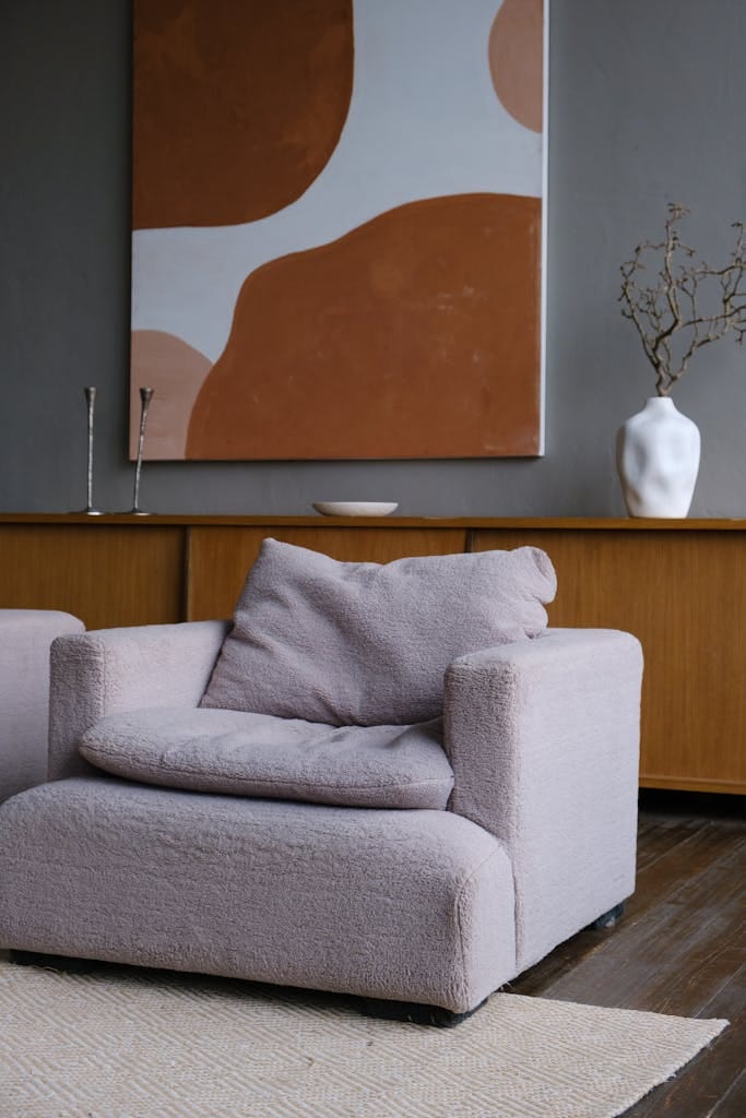 A contemporary interior featuring a plush armchair, wooden furniture, and abstract painting.